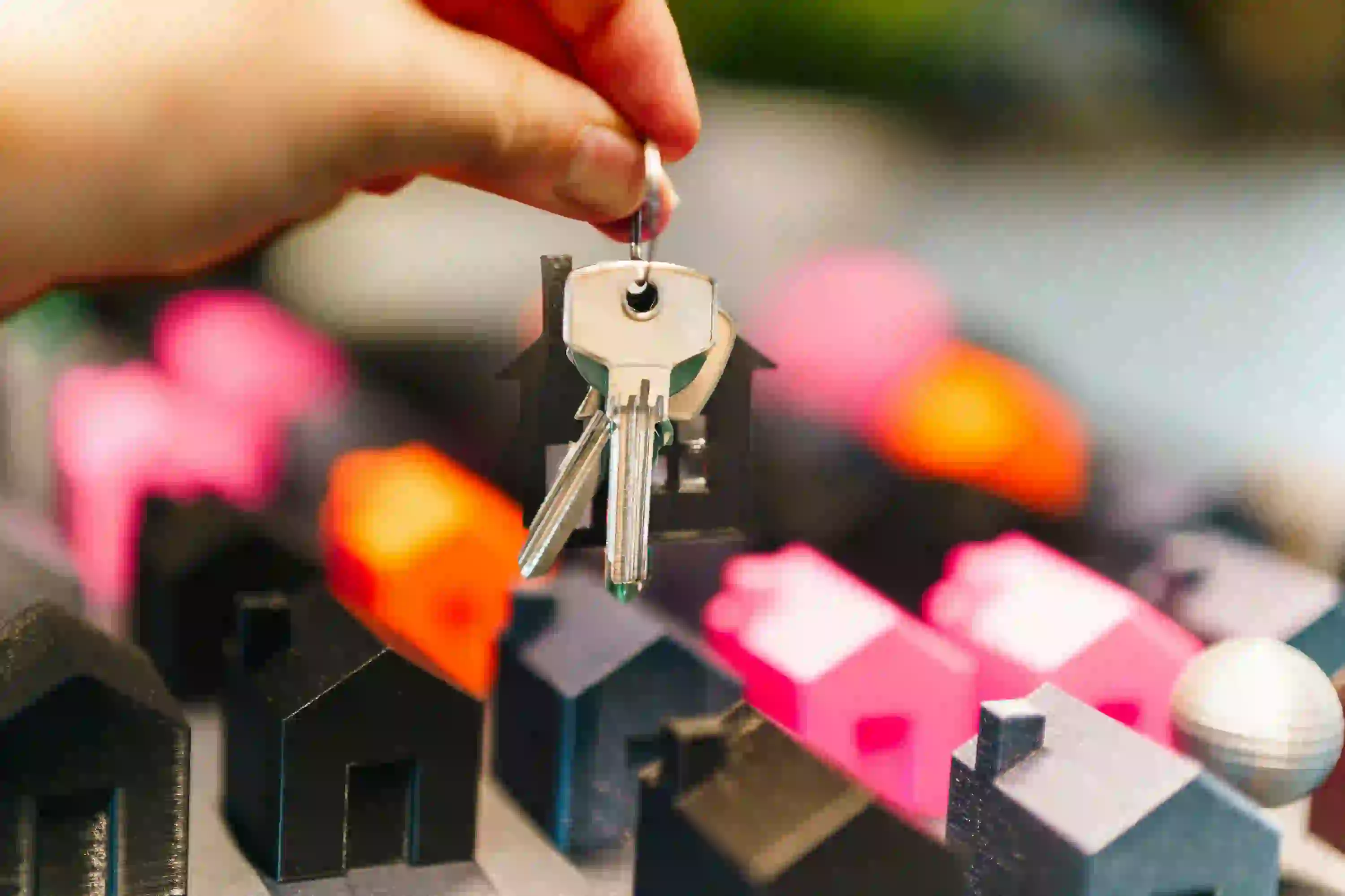 Hand holding house keys above miniature homes, real estate agent reputation management tips online.